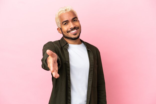 Young Colombian handsome man isolated on pink background shaking hands for closing a good deal