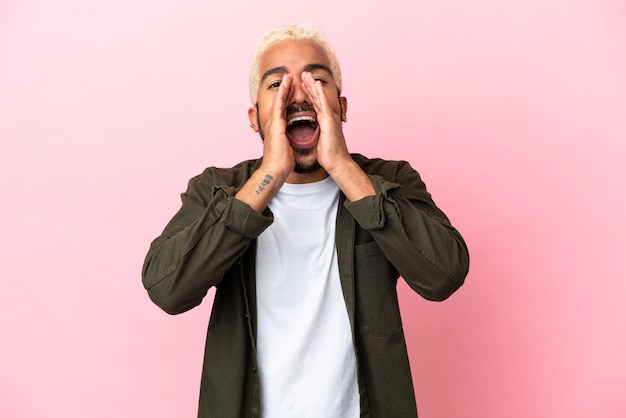 Young Colombian handsome man isolated on pink background shouting and announcing something