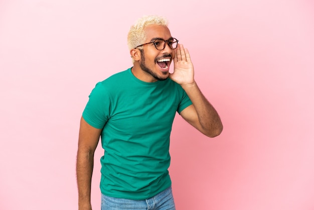 Young Colombian handsome man isolated on pink background shouting with mouth wide open to the side