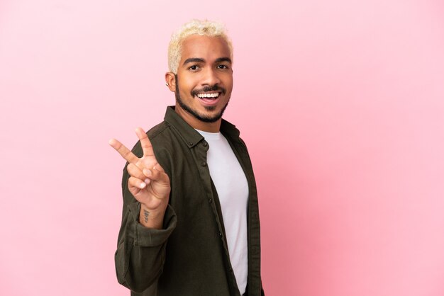 Young Colombian handsome man isolated on pink background smiling and showing victory sign