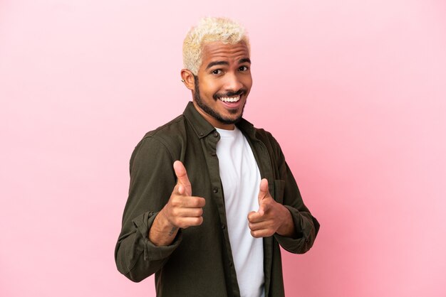 Young Colombian handsome man isolated on pink background surprised and pointing front