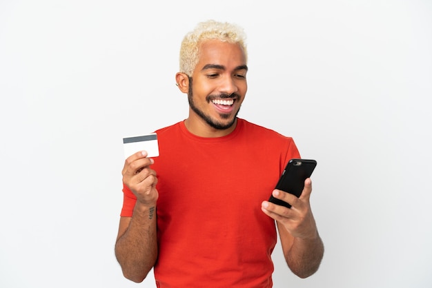 Young Colombian handsome man isolated on white background buying with the mobile with a credit card