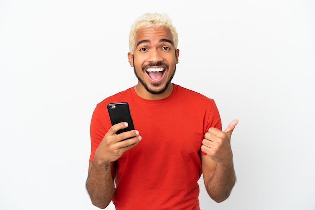 Photo young colombian handsome man isolated on white background using mobile phone while doing thumbs up