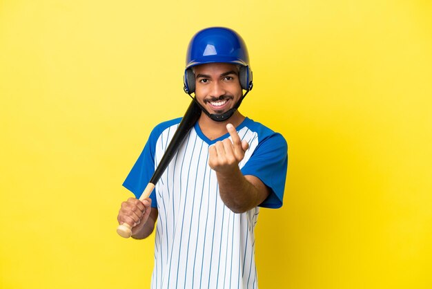 Young Colombian latin man playing baseball isolated on yellow background doing coming gesture