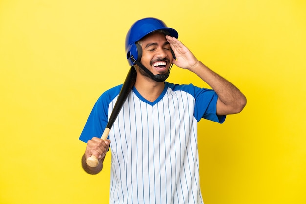 Young Colombian latin man playing baseball isolated on yellow background smiling a lot