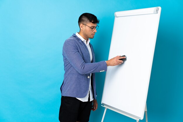 Young Colombian man isolated on blue giving a presentation on white board