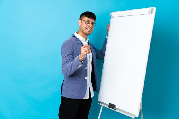 Young Colombian man isolated on blue giving a presentation on white board