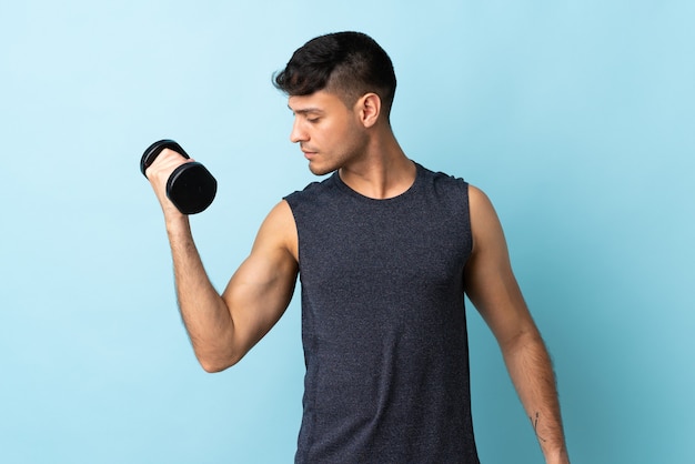 Young Colombian man isolated on blue making weightlifting