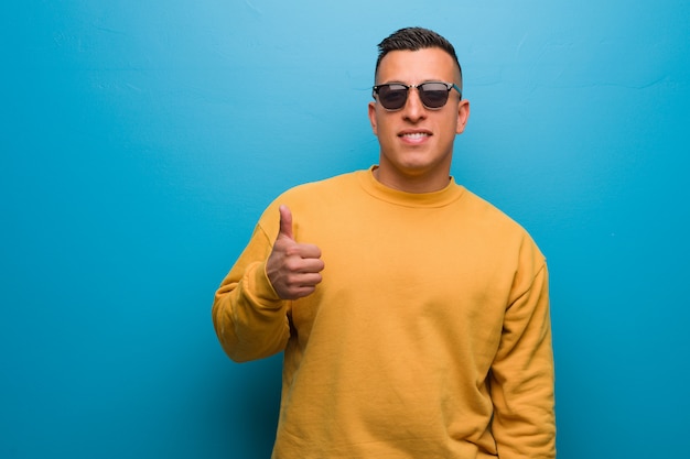 Young colombian man smiling and raising thumb up