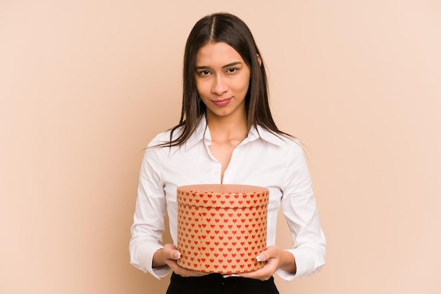 Young colombian woman holding a valentines day gift isolated on beige background