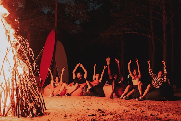 Young company sit in front of bonfire on beach