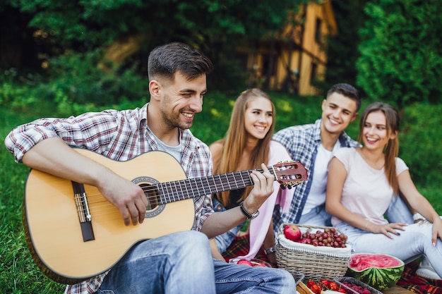 Foto una giovane compagnia di studenti trascorre i fine settimana nel parco e un ragazzo bruna suona la chitarra