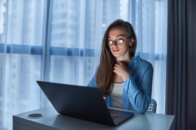 Young concentrated business woman freelancer in round glasses using computer