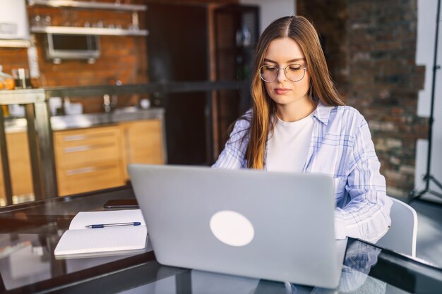 Young concentrated businesswoman in glasses and shirt working with laptop at home