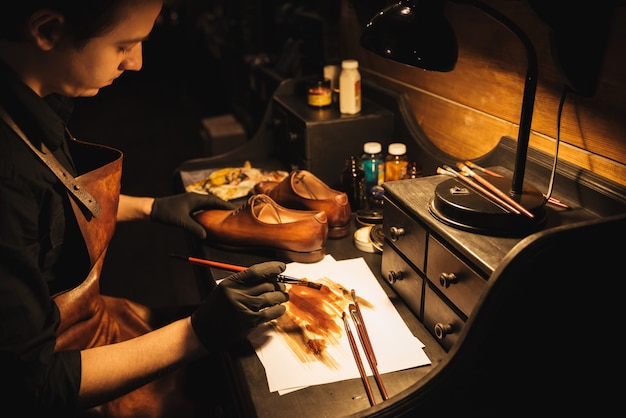 Young concentrated man shoemaker at footwear workshop.