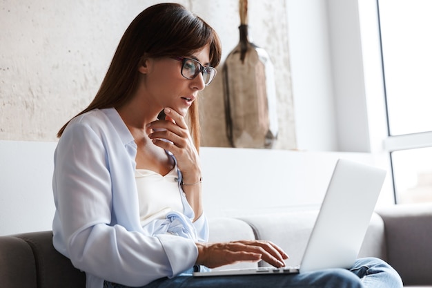 young concentrated serious business woman indoors at home on sofa in living room using laptop computer.