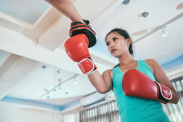 Young concentrated sport woman doing punching practicing with\
personal coach in gloves. asian girl taking boxing lesson learning\
with trainer indoor in gym. female boxer working out daily\
training.