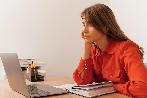 Young concentrated woman is looking thoughtfully at the laptop in the office