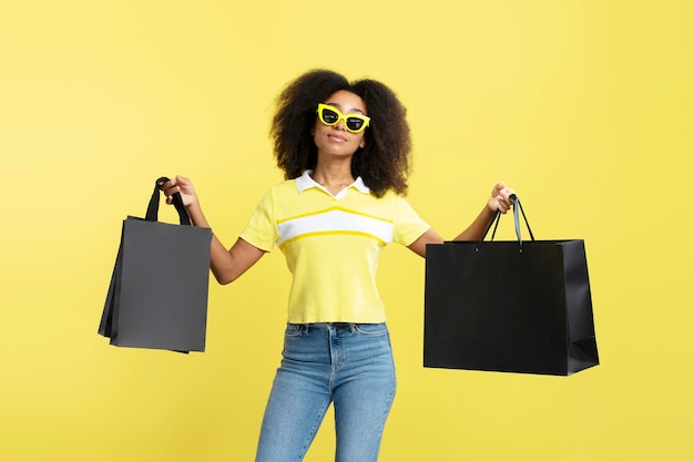 Young confident African American woman wearing stylish sunglasses holding black shopping bags