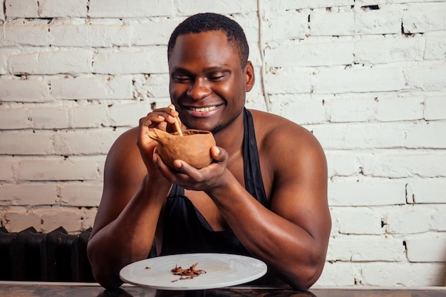 Young and confident afro american man in a black apron sculpts a potter from a clay pottery workshop. clay pot in the hand of the latin artist