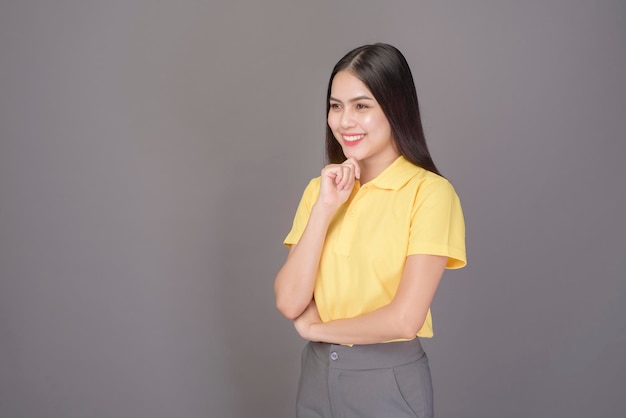 Молодая уверенная в себе красивая женщина в желтой рубашке находится на сером фоне студии
