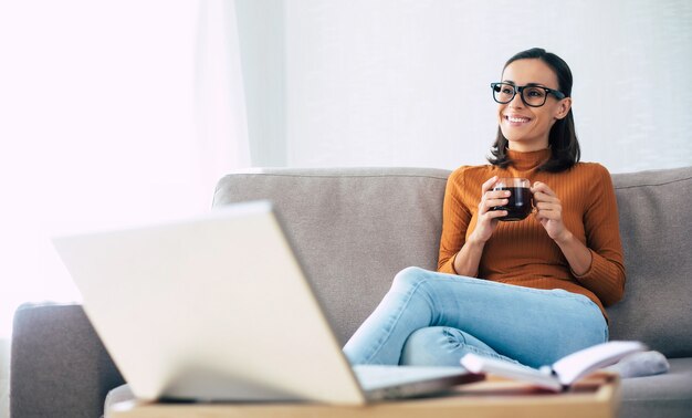 Young confident beautiful woman working with her laptop while sitting on the couch at home