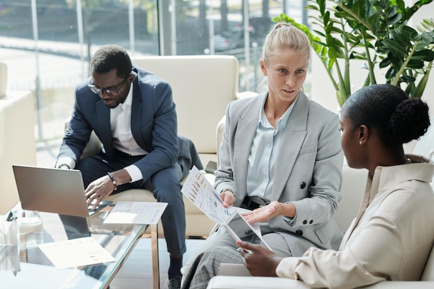 Young confident blond female economist showing financial data to colleague