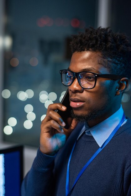 Молодой уверенный бизнесмен в элегантной повседневной одежде и очках, консультирующий клиента по мобильному телефону