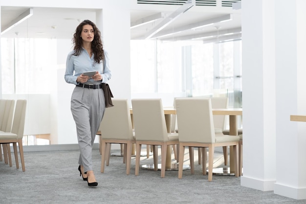 Young confident businesswoman in formalwear holding digital tablet