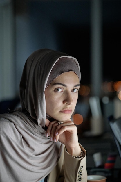 Young confident businesswoman in hijab sitting by workplace