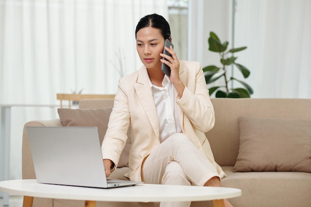 Young confident businesswoman with smartphone by ear sitting on couch