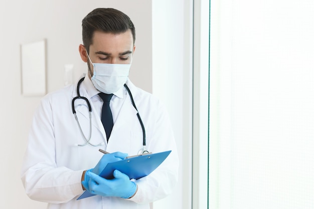 Young and confident doctor is holding the clipboard with a documents