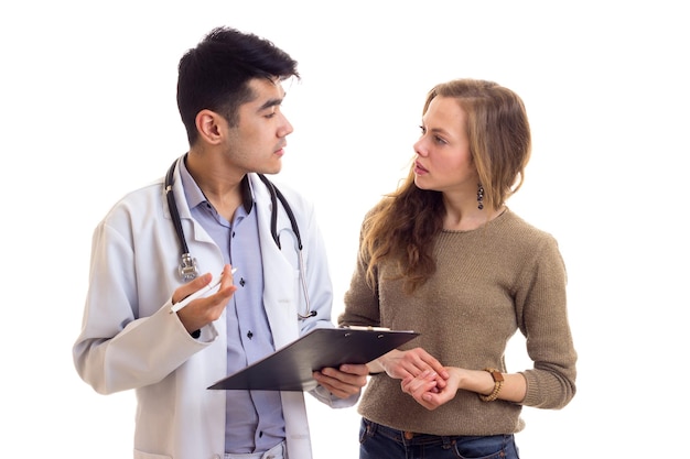 Young confident doctor in white gown with stethoscope looking throw papers with young nice woman