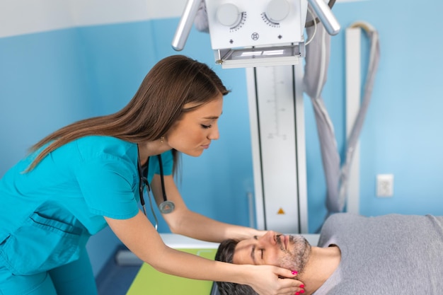 Young confident female doctor radiologist taking xray scan of male patient lying on the machine table Doctor standing near the patient during head X Ray procedure