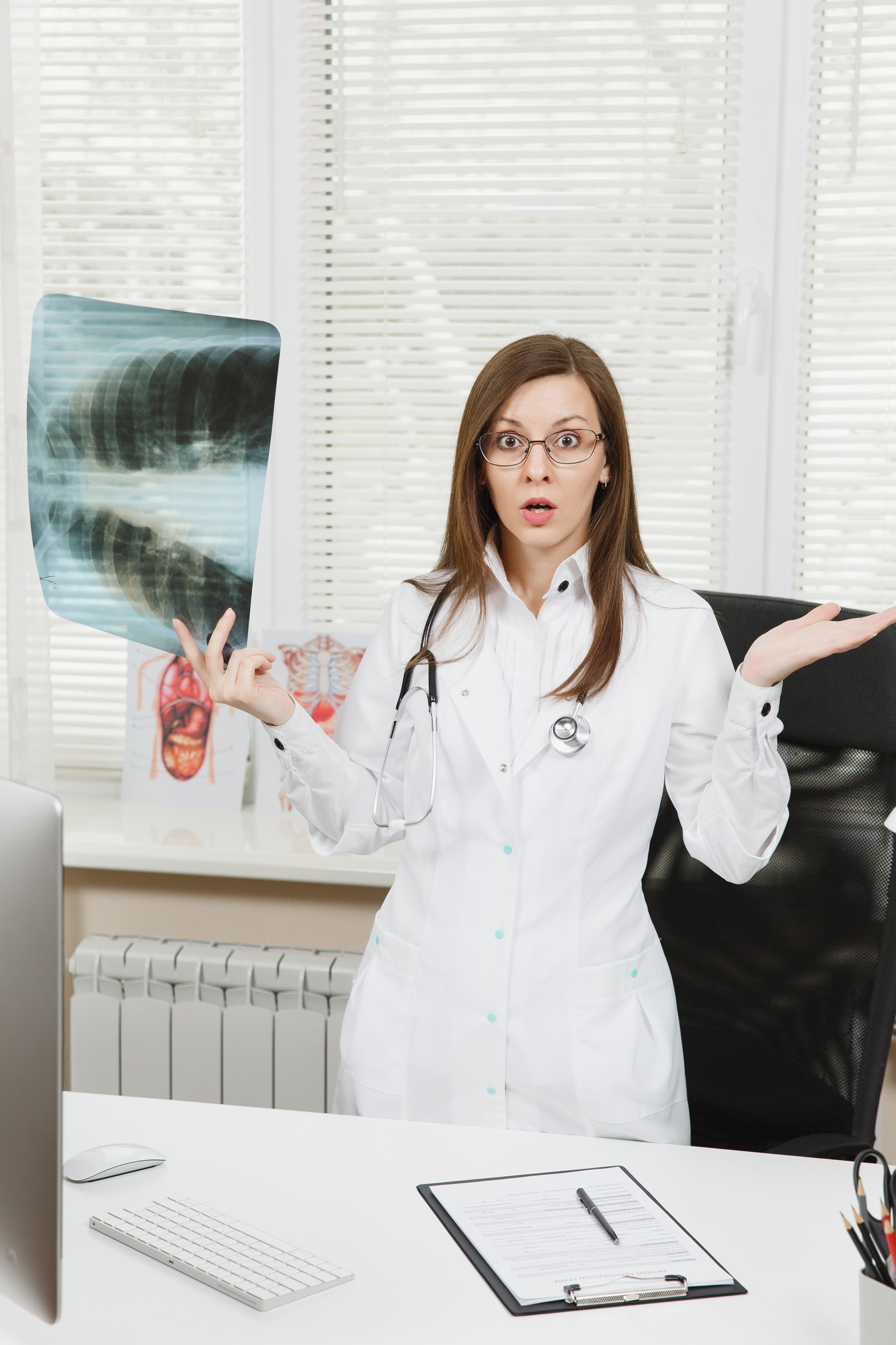 Young confident female doctor standing at desk, holding X-ray of lungs, fluorography, roentgen in light office in hospital