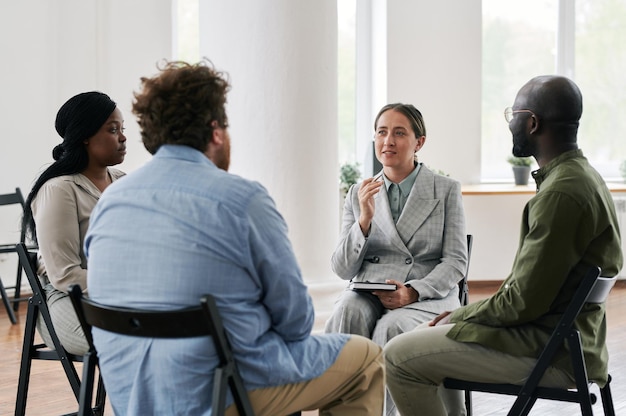 Young confident female psychologist in suit talking to group of patients