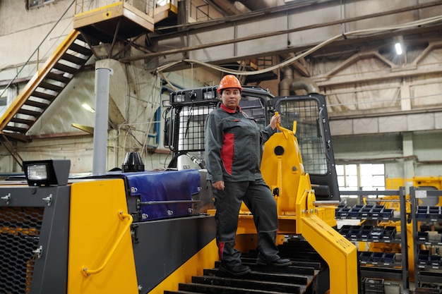 Young confident female worker standing on caterpillar of construction machine