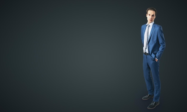 Young confident handsome man in blue suit isolated on blank dark grey backgound with empty place for your text or logo mockup