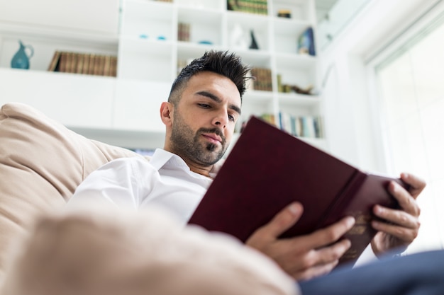 Young confident man reading book at modern home