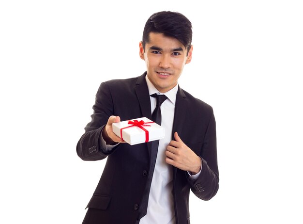 Young confident man with black hair in white shirt and black suit with tie holding a present