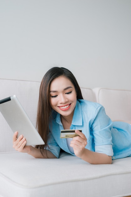 Young confident pretty woman working with digital tablet and credit card at home