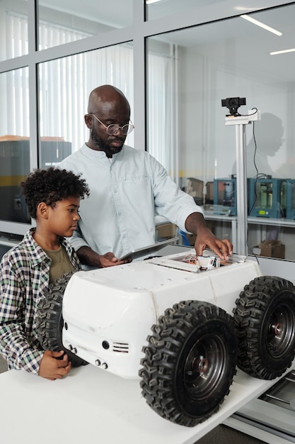 Young confident teacher with tablet explaining schoolboy how to control crawler