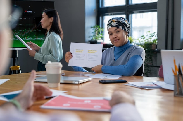 Young confident woman showing document with working strategies to colleague