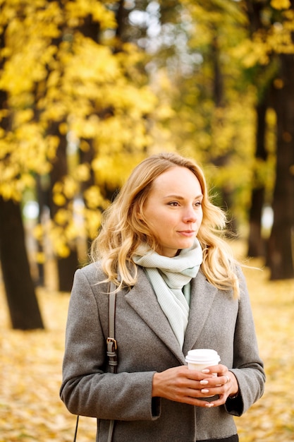 Young confident woman with coffee outdoors in sunny autumn day closeup portrait