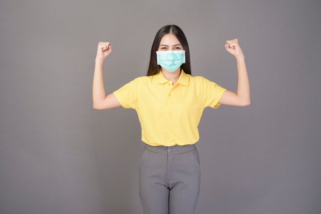 Молодая уверенная женщина в желтой рубашке носит хирургическую маску над серым