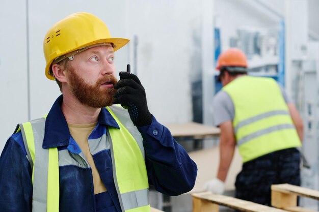 Giovane lavoratore fiducioso della fabbrica che parla in walkietalkie contro il collega