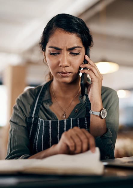 Young and confused business owner on the phone making a stock order for her cafe restaurant or coffee shop A female employee manager or store owner looking at a book of products or inventory