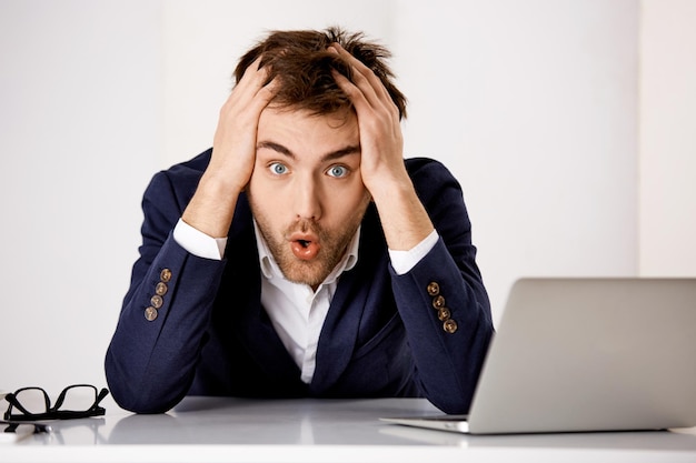 Young confused businessman sitting at the office desk