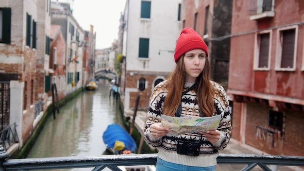 Молодая растерянная женщина, стоящая над водным каналом и смотрящая на карту Венеции, Италия