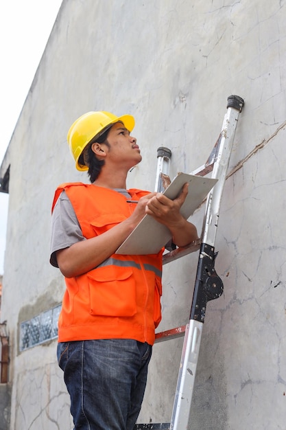 Young construction supervisor holding clipboard and checking while standing on stepladder Repair b